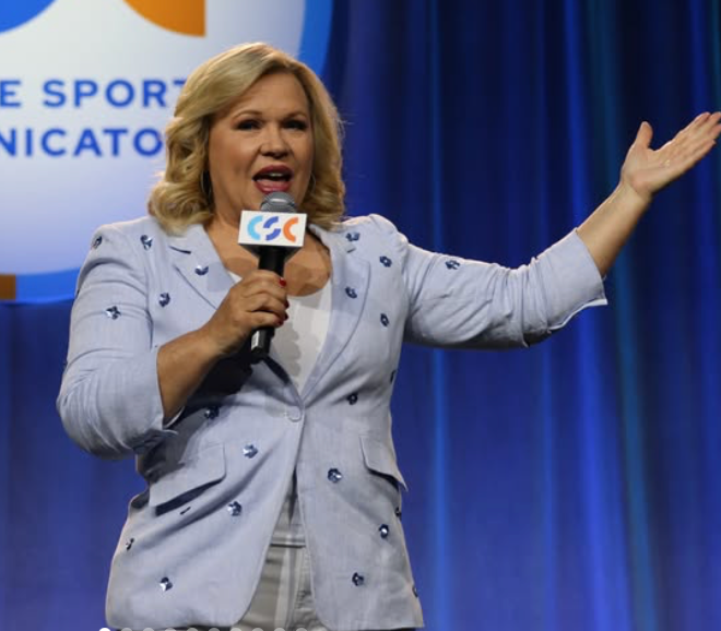 Holly Rowe reporting with a microphone in a light blue blazer